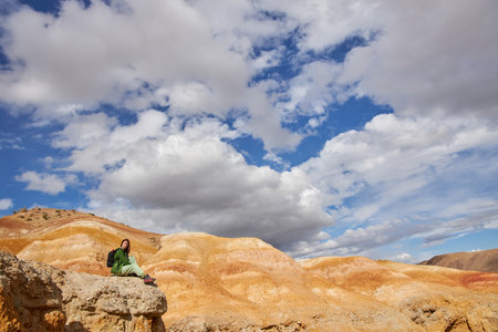 woman tourist sits in sand quarry against backdrop of sandy hills and cloudy sky. Sights of Russia, Siberia and Altai Republic, Field of Mars. Tourism, travel and adventure. Kosh-agach, Chagan-Uzunの写真素材
