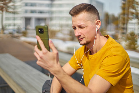 man student with a smartphone in his hands and headphones, against the backdrop of the university buildingの写真素材