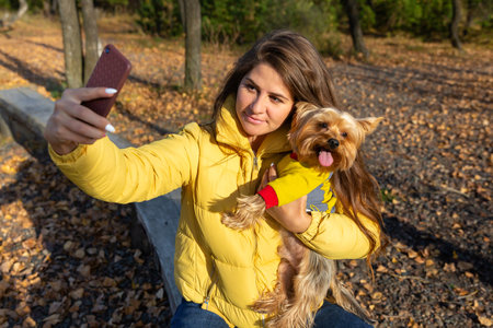 a woman takes a selfie on a smartphone with her small dog yorkshire terrierの写真素材