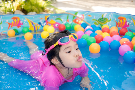A baby girl in pink suit playing water and balls in blue kiddie poolの写真素材