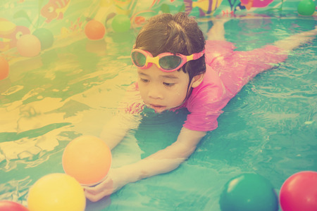 A baby girl in pink suit playing water and balls in blue kiddie pool - vintage effectの写真素材
