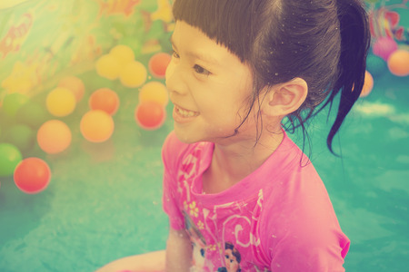 A baby girl in pink suit playing water and balls in blue kiddie pool - vintage effectの写真素材
