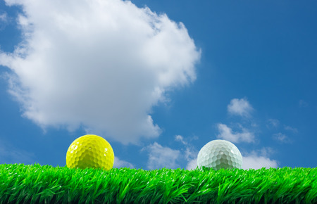 White and yellow golf balls on green artificial grass in blue sky backgroundの写真素材