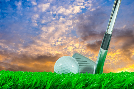 White golf ball and iron club on green artificial grass in evening sky background