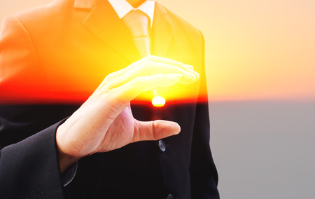 Double exposure businessman in dark gray suit and the sun. The man trying to catch the sun in his hand.の写真素材