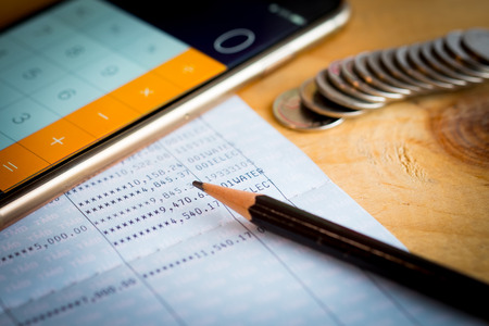 Savings account bank book, pencil and smartphone used as calculator on wooden tableの写真素材