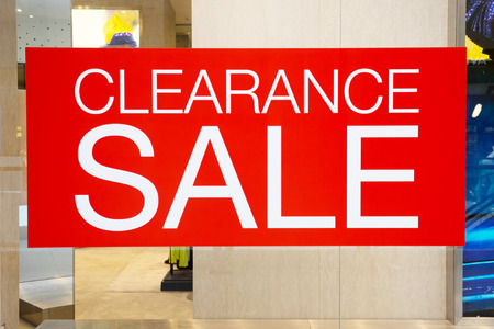 Clearance sale cut out label display on glass window along side with plastic model doll in clothes store in fashion mall