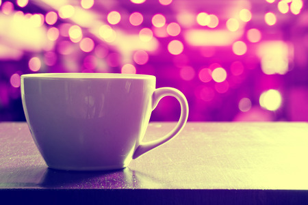 Hot coffee in white cup on wooden table in coffee shop or cafe. Purple light with vintage effect.