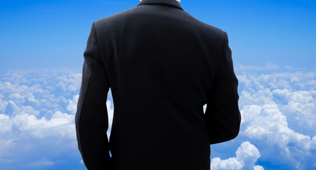 Back side of businessman in dark gray suit when he is looking to blue sky above the sea of clouds. Looking for success.の写真素材
