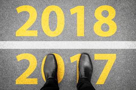 Businessman in black shoes standing at the line between last year 2017 and new year 2018.の写真素材