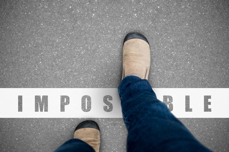 One wearing jeans and brown suede shoes walking over the impossible line representing positive can do and everything possible concept.の写真素材