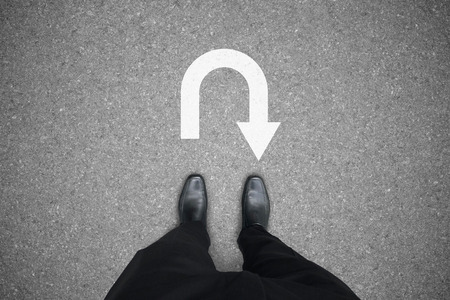 Businessman in black shoes standing at the u turn sign on the road. No way to go and have to turn...