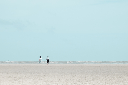 Two women walking on the beach to the calm sea. Pastel color effect.の写真素材