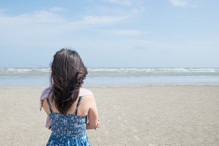 Woman in blue dress and pink scarf standing on the beach crossing one's arm alone and feeling lonely.の写真素材