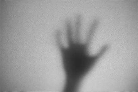 Shadow of hand the white frosted glass representing dangerous, fear, help, horror and scary.の写真素材