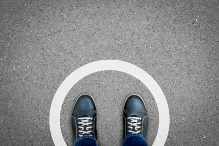 Black shoes standing in white circle on the asphalt concrete floor. Concept of limit, boundary,...