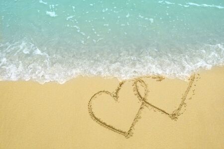 Two hearts drawn on the sand beach being wash away by a wave representing divorce, breakup concept.の写真素材