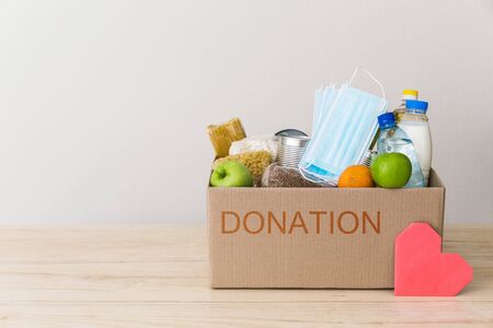 Charity donation box made of cardboard with food: oil, fruits, cereals, canned food. White background, table in the kitchen. Pink heart postcard. Copy space for textの写真素材