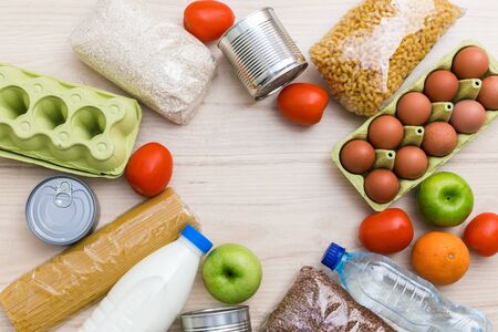 Charity donation food set: oil, fruits, cereals, canned food. Wooden kitchen table background in Scandinavian interior. Flatlay, top view. Copy space for textの写真素材