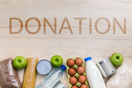 Charity donation food set with oil, milk and water, herbs, apples and oranges, cereals and canned food, rice and pasta. Wooden kitchen table background in Scandinavian interior. Flatlay, top viewの写真素材