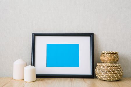 Mockup of a black horizontal photo frame with Passepartout. The light interior in the Scandinavian style. Composition on the table, shelf. Wicker round baskets, white candlesの写真素材