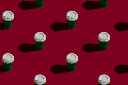 Bleached paper disposable coffee mug with a white plastic lid. Seamless pattern on a solid red background. Concept for coffee with you to take away. Bright banner design elementの写真素材