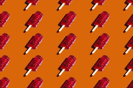 Red with black shavings on a stick. Isolated seamless pattern on a solid orange background. Ice cream concept on a hot summer day. Bright banner design elementの写真素材