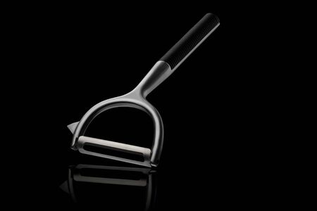 Metal chrome vegetable peeler. Kitchen accessory for cooking on a black isolated backgroundの写真素材
