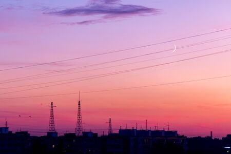 Pink orange purple sunset over the city. Multicolored sky and black silhouette of tall buildings of the metropolis. Radio towers and TV antennas. Gentle sky and the moonの写真素材