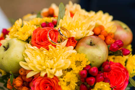 Wedding rings of the bride and groom on the background of a bouquet. Wedding concept. Autumn bouquet with applesの写真素材