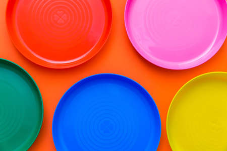 Children's unbreakable multicolored dishes, serving for a children's holiday. Isolated on an orange...