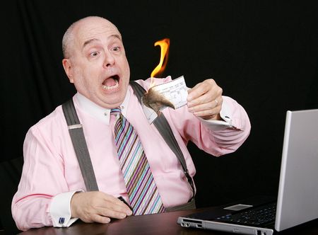 surprised businessman watching his paycheck go up in smokeの写真素材