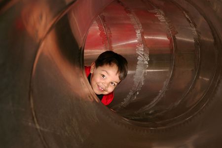 young male child playing sliding in a metal tube slide on a playgroundの写真素材