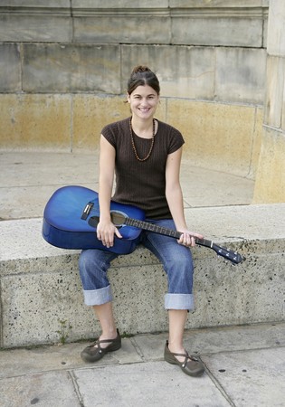 full length portrait of one woman sitting with her blue guitar outdoors