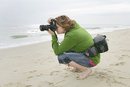 a redhead woman squatting to take a photo on the beach