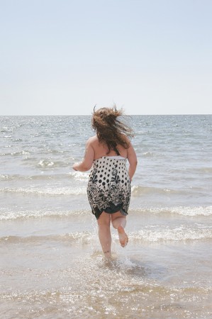 one attractive plus size model running in the water edge at the beach getting wetの写真素材