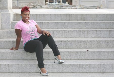 one young African American female smiling and happy sitting on stone stairs outdoorsの写真素材