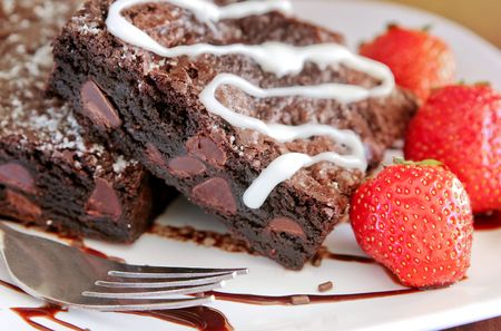 two fresh, delicious looking chocolate brownies on a white plate with fresh strawberries closeup angleの写真素材