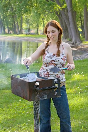 Teenage girl cooks hamburger patties on a barbecue grill at a park. Vertical format.の写真素材