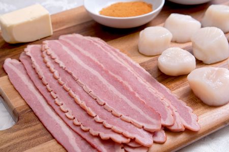 mise en place on a wooden cutting board for a batch of bacon wrapped scallops before being cookedの写真素材