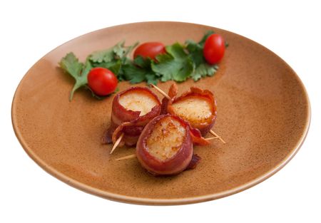 plate of three bacon wrapped scallops with cherry tomato garnish on a brown plate isolated on whiteの写真素材