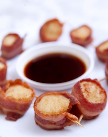 small group of scallops wrapped in turkey bacon with sauce bowl on a white plateの写真素材