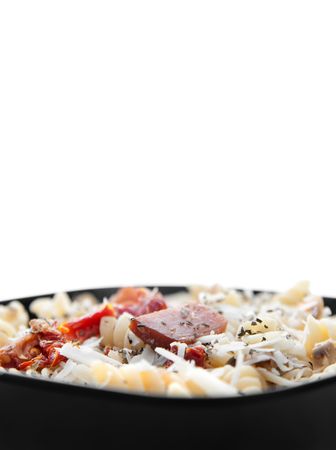low angle of bacon and sun dried tomato pasta with mushrooms and parmesan cheese in a black bowl. plenty of vertical copyspace for textの写真素材