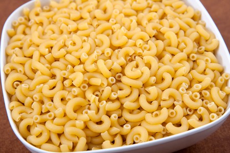 large white bowl of uncooked yellow elbow macaroni pasta closeupの写真素材