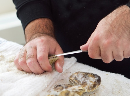 man shucking an oyster with a knife closeup with hands