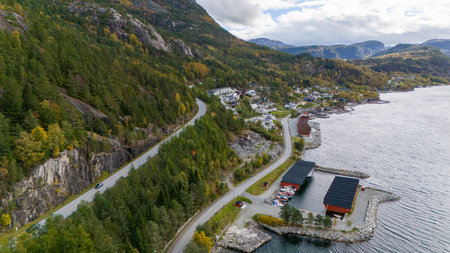 Aerial view of a scenic coastal village with houses surrounded by autumn foliage, overlooking a calm body of water and distant islands in Norwegian fjords.の写真素材