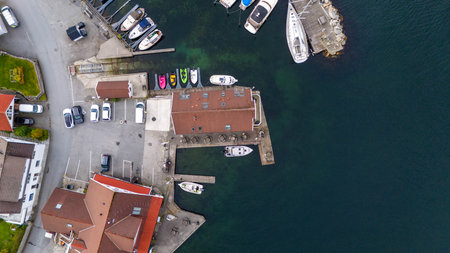 Aerial view of a marina with boats docked along the pier, surrounded by buildings and parked cars.