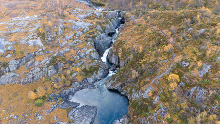 Aerial view of a stunning waterfall cascading down rocky cliffs into a deep blue pool surrounded by...