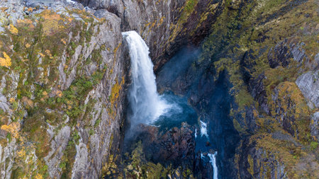 Aerial view of a stunning waterfall cascading down rocky cliffs into a deep blue pool surrounded by...