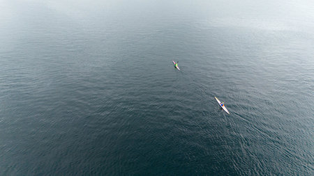 Aerial view of two kayakers paddling on a calm, expansive fjord.
